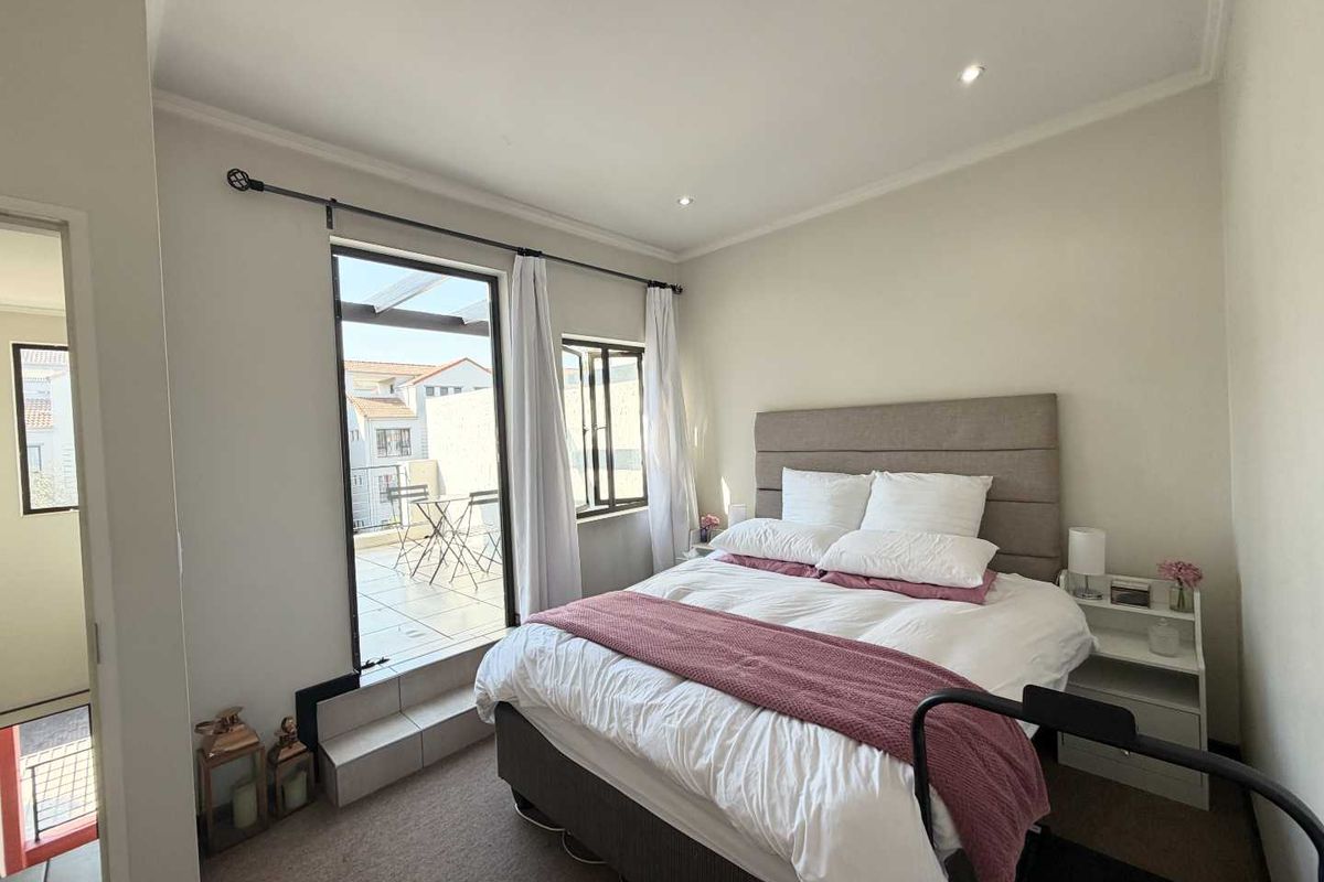 A well-lit bedroom featuring carpeted flooring, recessed downlights, and direct access to a private balcony through a sliding glass door.