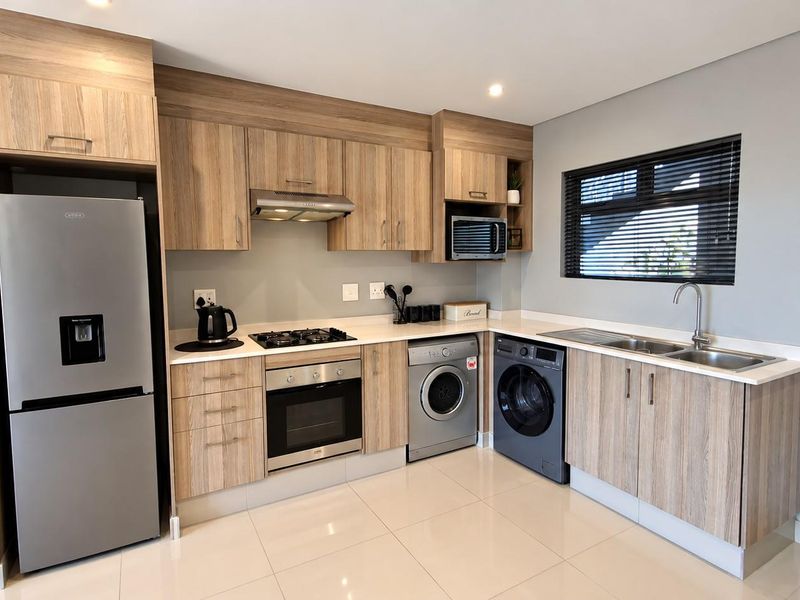 Modern kitchen featuring wood-finish cabinetry, stone countertops, integrated appliances, gas hob, electric oven, and tiled flooring with a window for natural light.