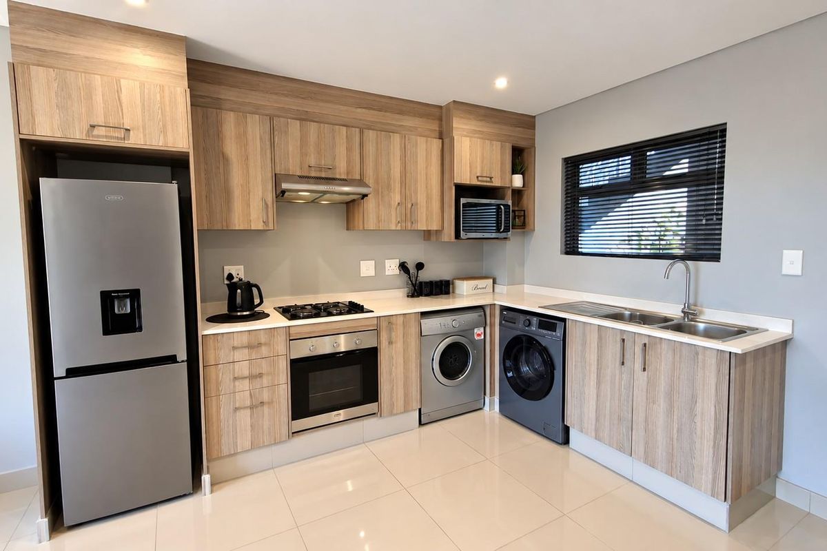 Modern kitchen featuring wood-finish cabinetry, stone countertops, integrated appliances, gas hob, electric oven, and tiled flooring with a window for natural light.