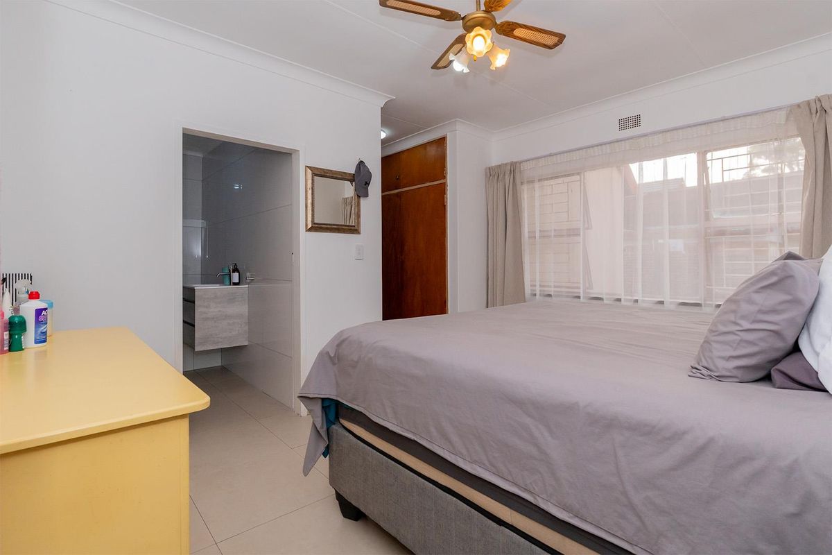 A bedroom featuring tiled flooring, built-in wooden wardrobe, and an en-suite bathroom with modern vanity.