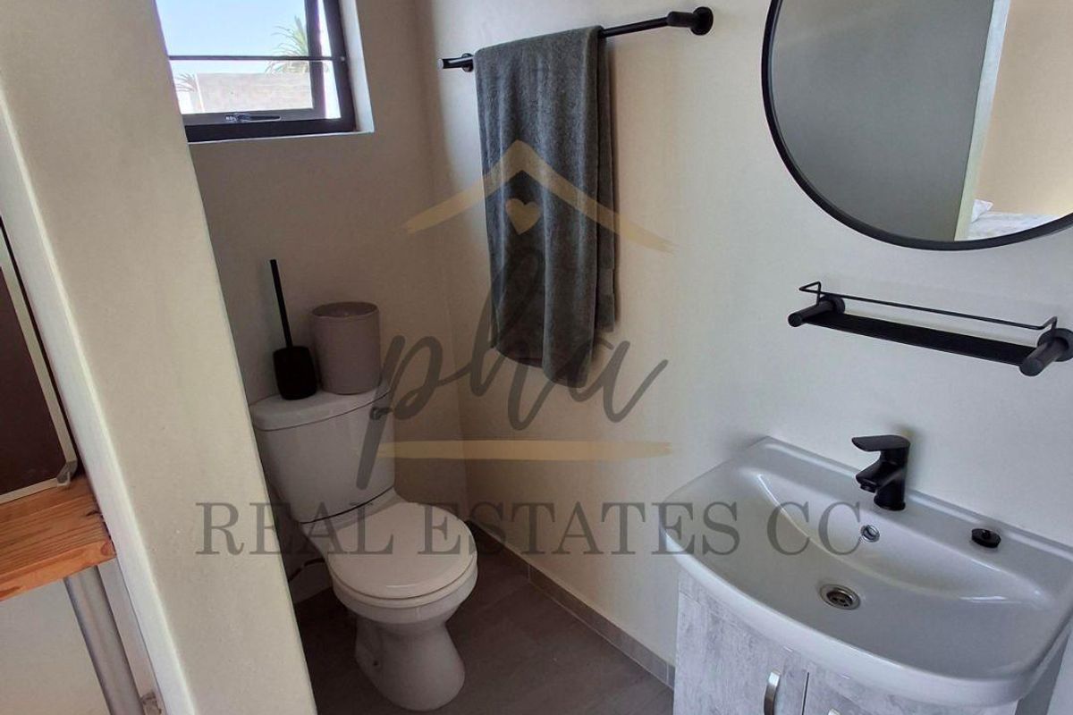 A compact, modern bathroom featuring a vanity with a basin, a toilet, and a circular wall-mounted mirror.