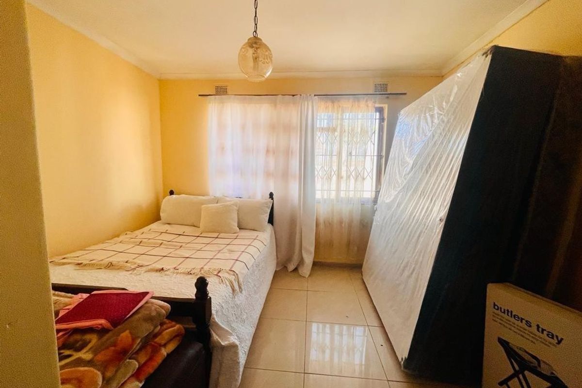 A functional bedroom featuring tiled flooring, a window with a security gate, and a central pendant light fixture.