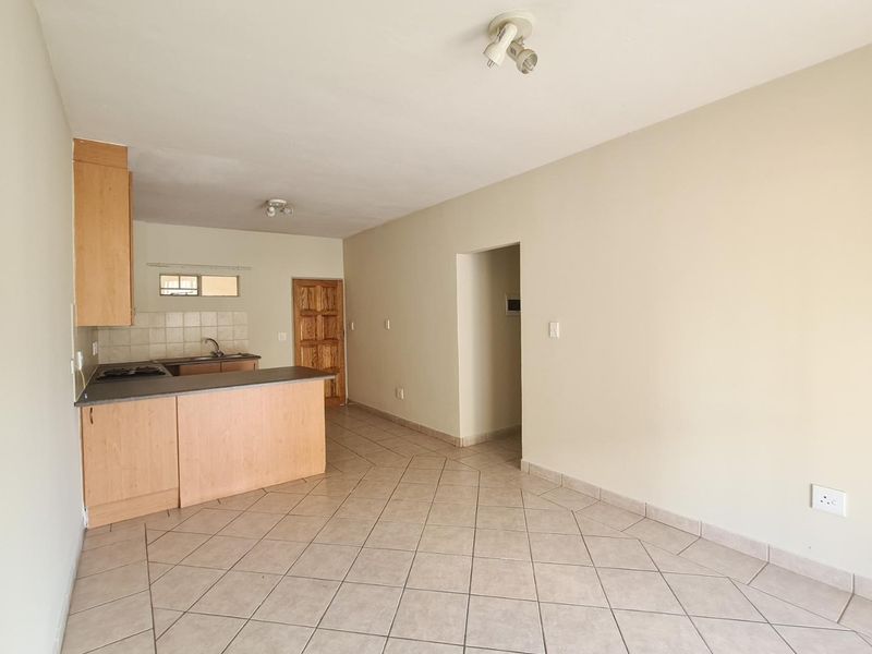 Open plan living and kitchen area featuring tiled flooring, wooden cabinetry, built-in hob, and a breakfast counter in a neutral, vacant space.