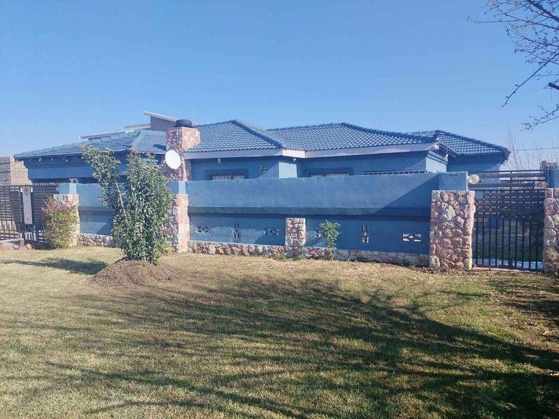 Front view of a residential property featuring a blue exterior, stone-clad boundary wall, and a tiled roof with a secure gated entrance.