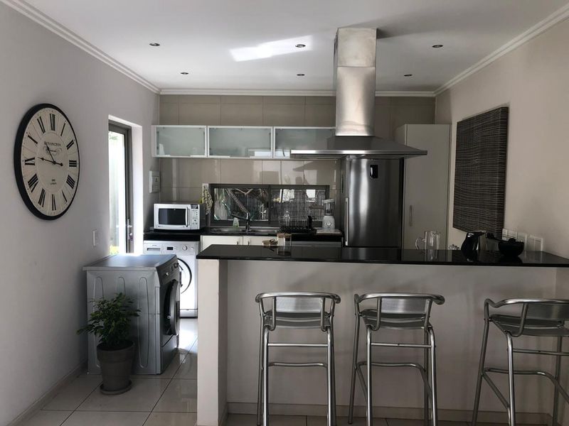A functional kitchen featuring a granite breakfast bar, stainless steel extractor fan, tiled backsplash, and modern recessed lighting.