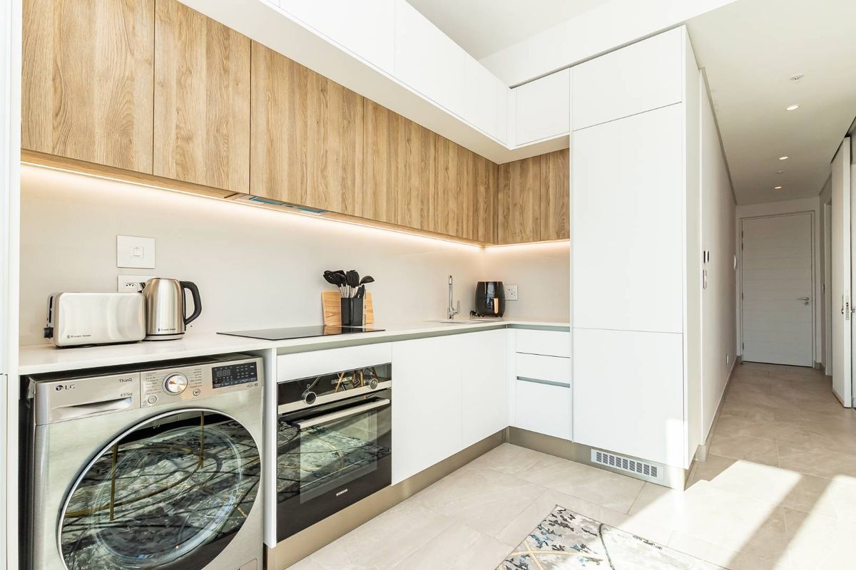 Modern, compact kitchen featuring sleek white cabinetry, wood-grain upper cupboards, integrated appliances, and high-quality finishes throughout.