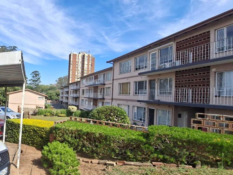 Exterior view of a multi-story apartment complex featuring brick facade, private balconies with metal railings, and landscaped garden areas.