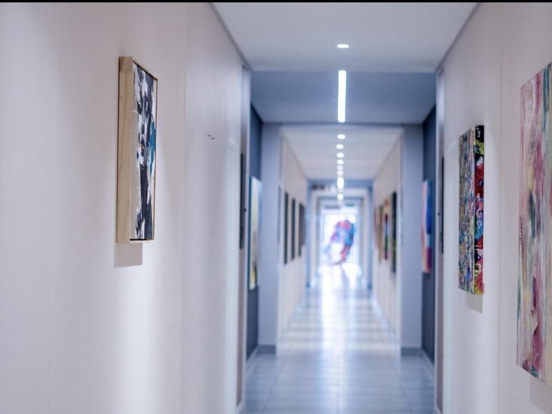 A long, well-lit apartment hallway featuring modern recessed linear lighting and clean tiled flooring, creating a bright and spacious transition area.