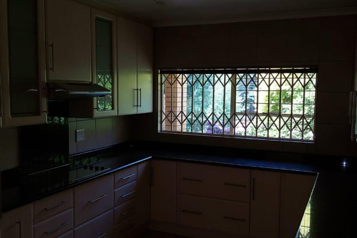 A functional kitchen featuring dark countertops, built-in cabinetry, an integrated oven, and a window with security bars overlooking the garden.