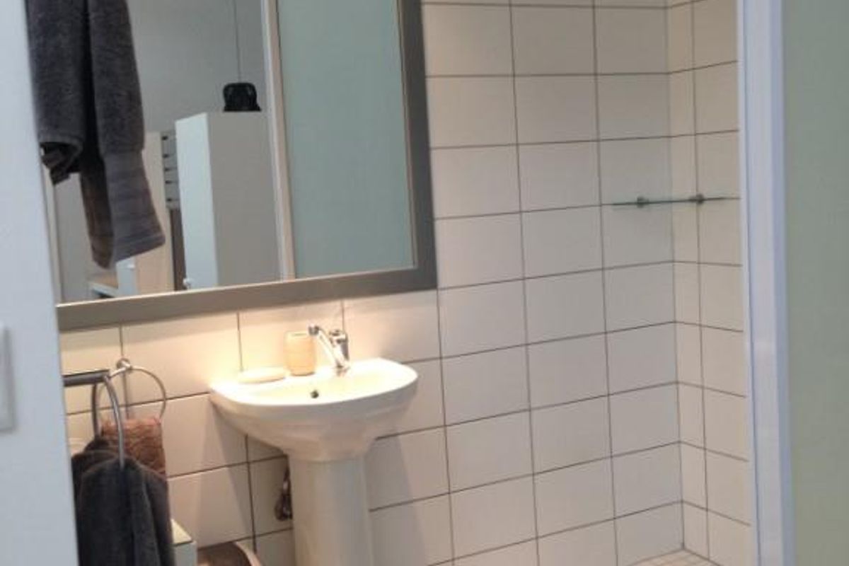 A modern bathroom featuring a pedestal sink, a large framed mirror, and a walk-in shower with white wall tiles and a rainfall showerhead.