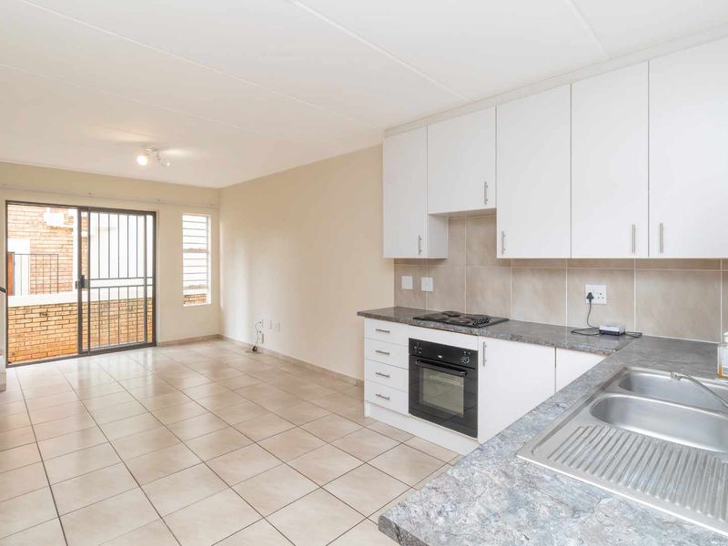 Open-plan kitchen and living area featuring tiled floors, built-in cabinetry, integrated oven and hob, and access to an outdoor balcony through a sliding door.