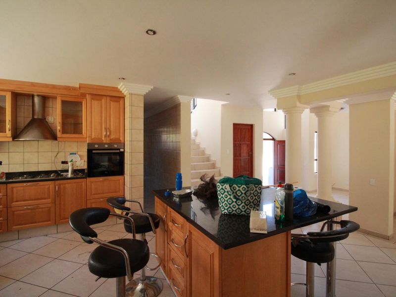 Open plan kitchen featuring wooden cabinetry, a granite island, and tiled flooring, flowing into a spacious living area with decorative columns.