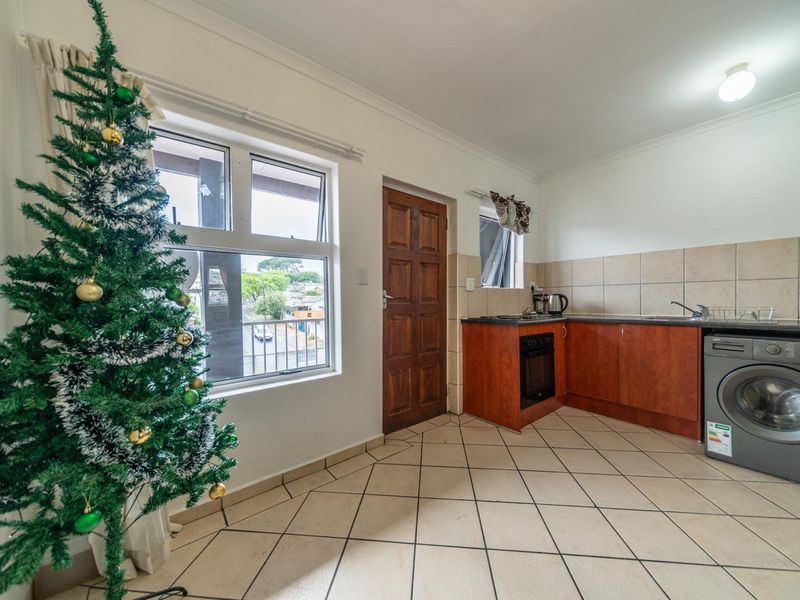 Compact kitchen featuring tiled flooring, built-in cabinetry, a tiled backsplash, and integrated appliances, with direct access to an exterior door.