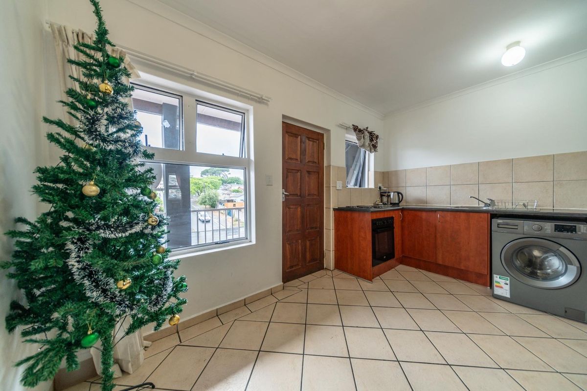 Compact kitchen featuring tiled flooring, built-in cabinetry, a tiled backsplash, and integrated appliances, with direct access to an exterior door.