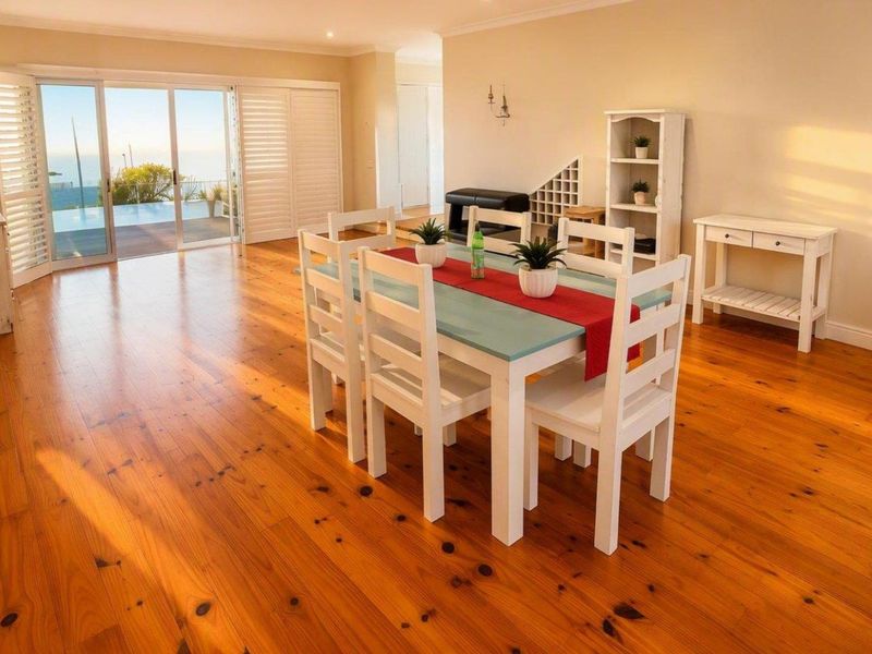 Spacious open-plan living and dining area featuring warm timber flooring and large sliding doors opening to an outdoor pool deck.