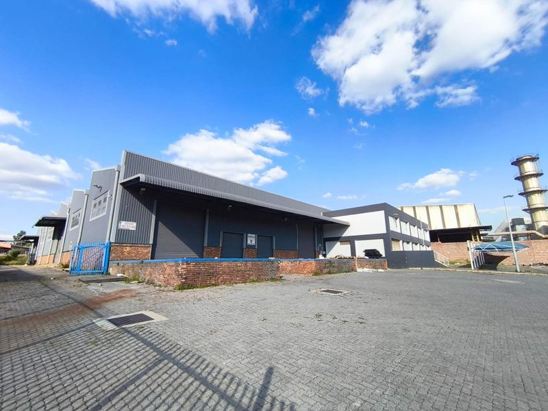 Industrial warehouse exterior featuring a loading dock, roller shutter doors, and a spacious paved yard area suitable for logistics and distribution operations.