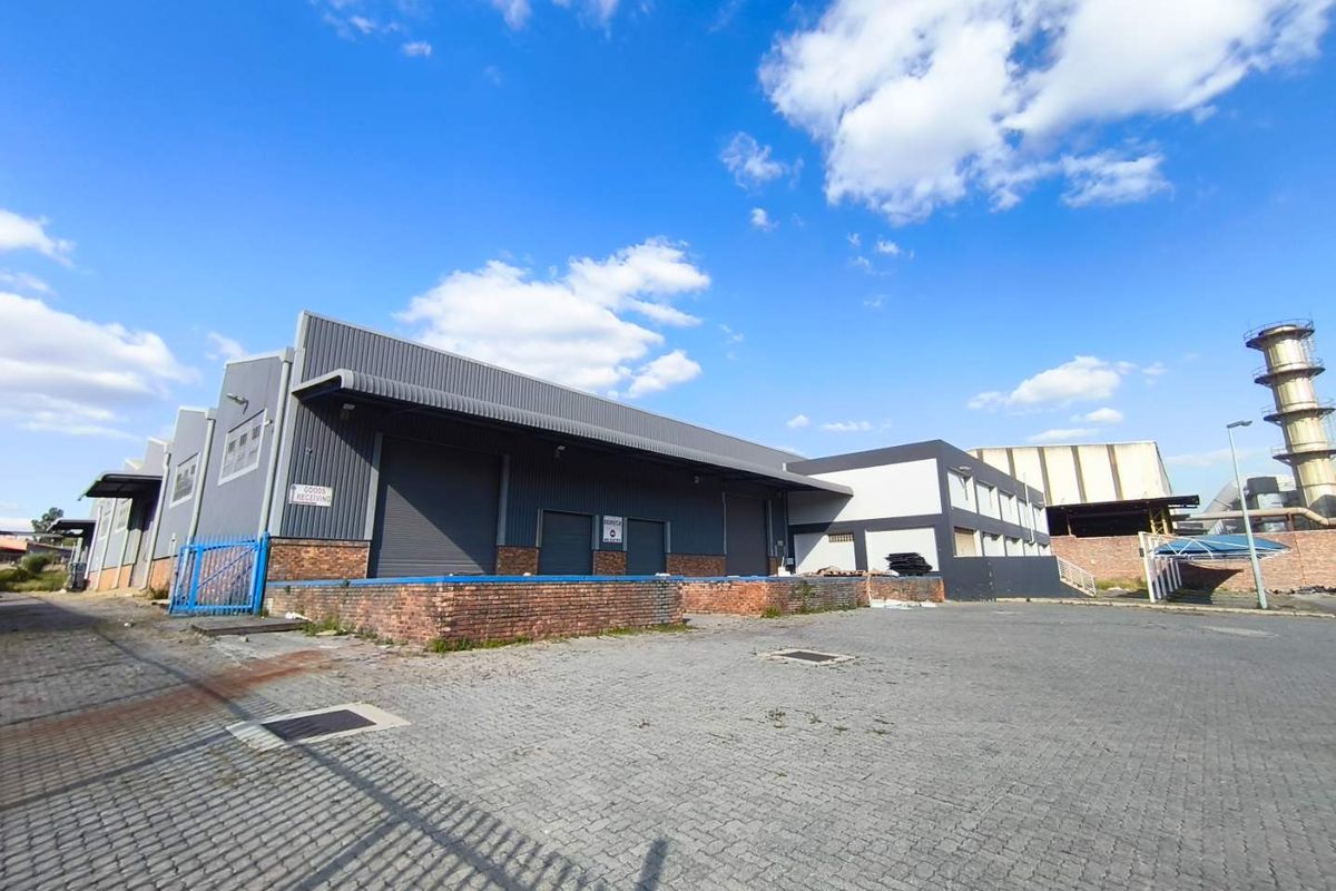 Industrial warehouse exterior featuring a loading dock, roller shutter doors, and a spacious paved yard area suitable for logistics and distribution operations.