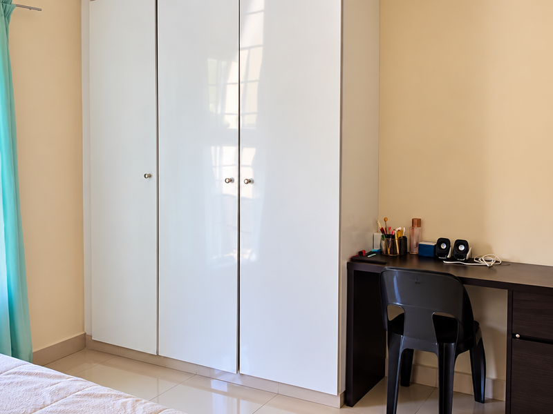 A well-lit bedroom featuring neutral walls, tiled flooring, and a modern white built-in wardrobe.
