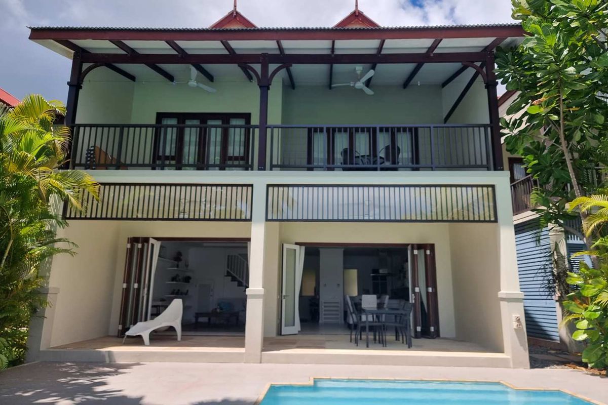 Rear view of a two-story maison de ville featuring a ground floor patio, swimming pool, and a spacious upper-level balcony with timber framing.