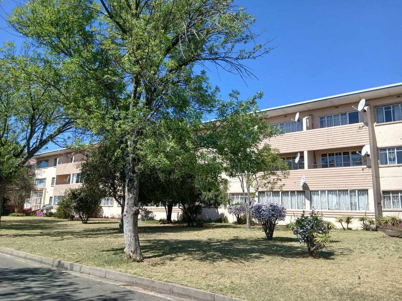 A multi-story apartment building exterior featuring balconies and a well-maintained garden area in front.