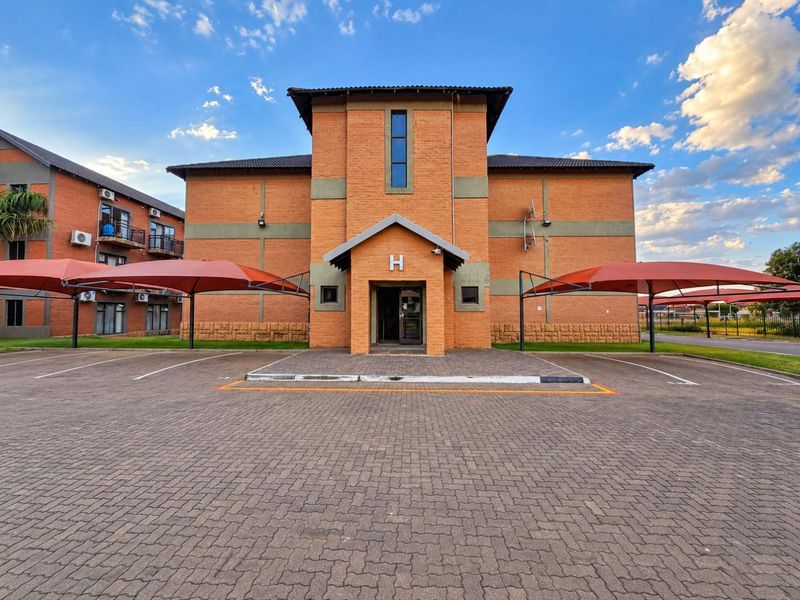Front elevation of a face brick apartment building featuring a paved parking area with shade cloth carports.