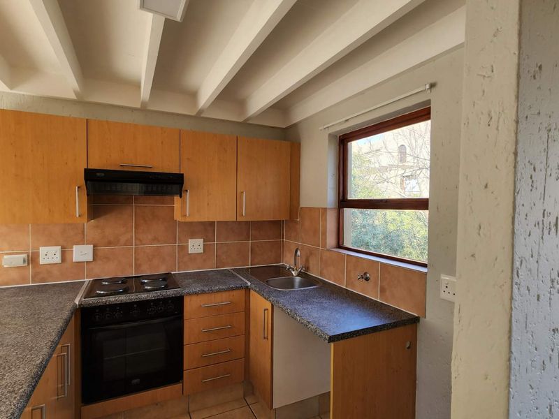 A functional kitchen featuring wooden cabinetry, granite-look countertops, an electric stove with extractor fan, and a tiled backsplash with exposed ceiling beams.