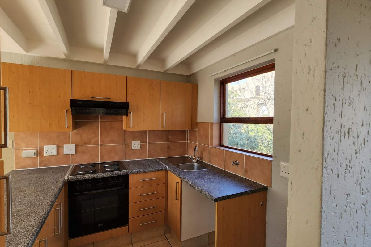 A functional kitchen featuring wooden cabinetry, granite-look countertops, an electric stove with extractor fan, and a tiled backsplash with exposed ceiling beams.