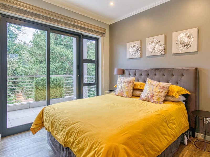A well-maintained bedroom featuring laminate flooring, recessed lighting, and large sliding glass doors that provide direct access to a private balcony.