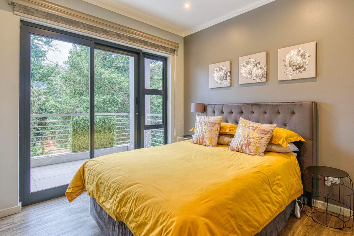 A well-maintained bedroom featuring laminate flooring, recessed lighting, and large sliding glass doors that provide direct access to a private balcony.