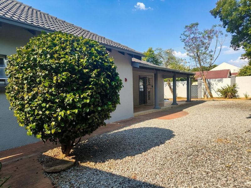 A view of the rear exterior featuring a covered patio with support columns, a tiled roof, and a gravel yard area.