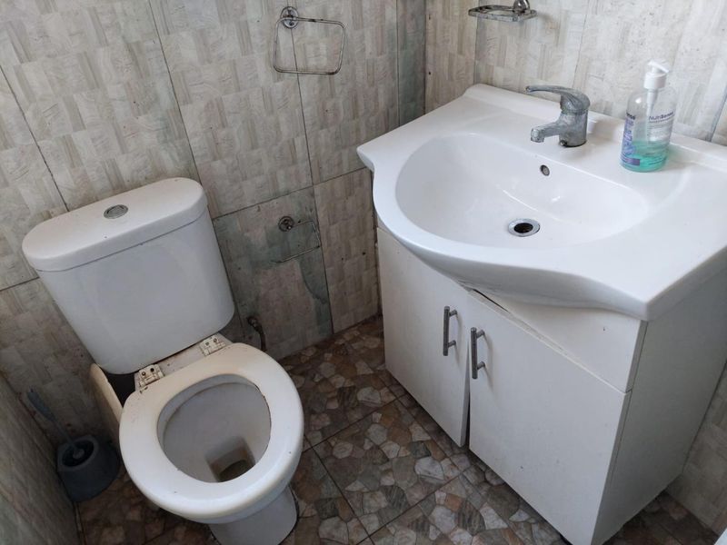 Compact bathroom featuring a vanity cabinet with basin and a standard toilet, finished with tiled walls and flooring.