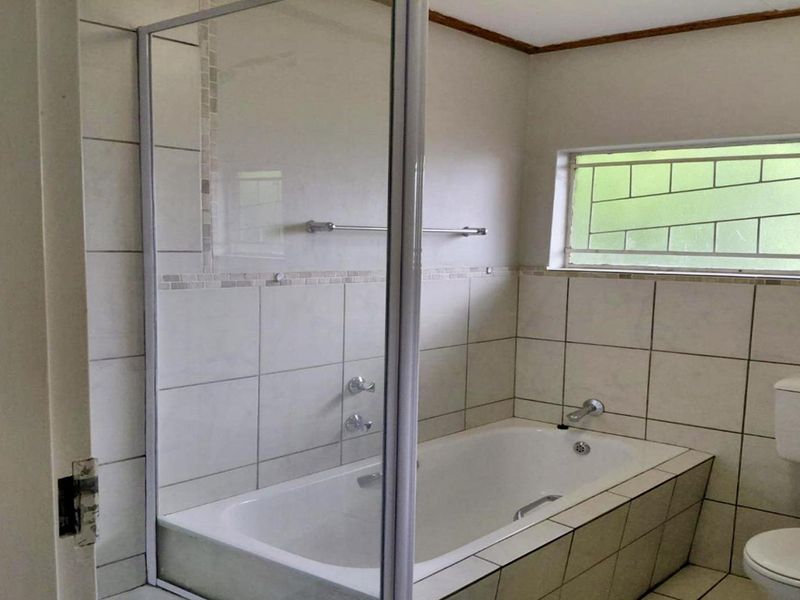 A functional bathroom featuring a built-in bathtub with a glass screen, tiled walls, a pedestal basin, and a toilet.