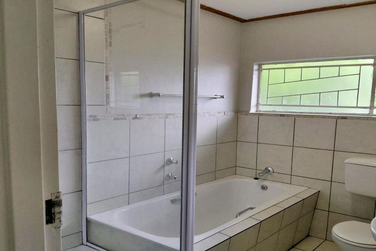 A functional bathroom featuring a built-in bathtub with a glass screen, tiled walls, a pedestal basin, and a toilet.