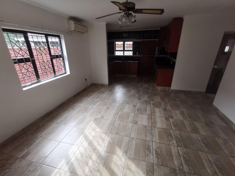 An open-plan living and kitchen area featuring tiled flooring, a ceiling fan, and a wall-mounted air conditioning unit.