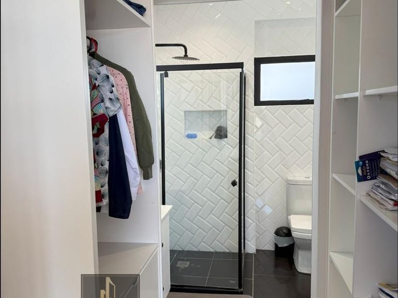 A modern bathroom featuring a walk-in shower with black frame, herringbone wall tiling, and an adjacent walk-in closet with built-in shelving.