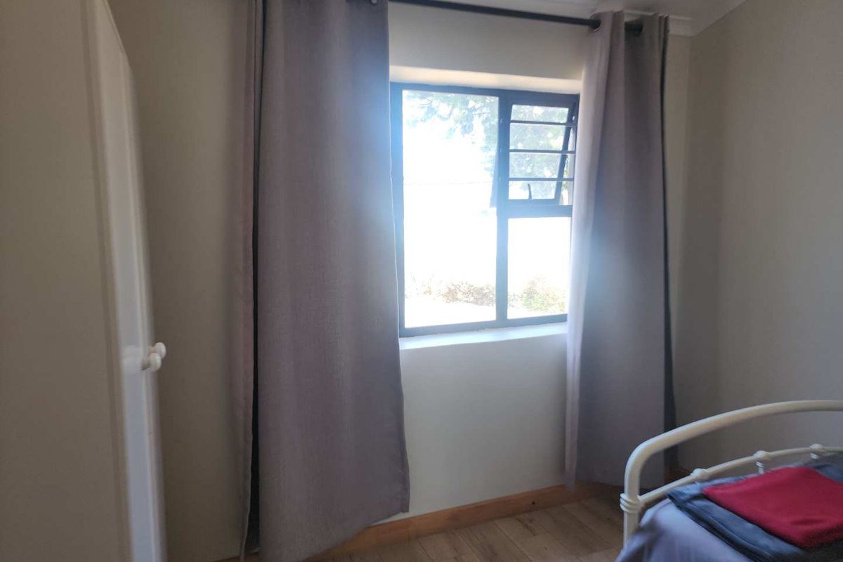 A bedroom featuring light-toned walls, timber-look flooring, and a window with a metal frame, providing natural light.