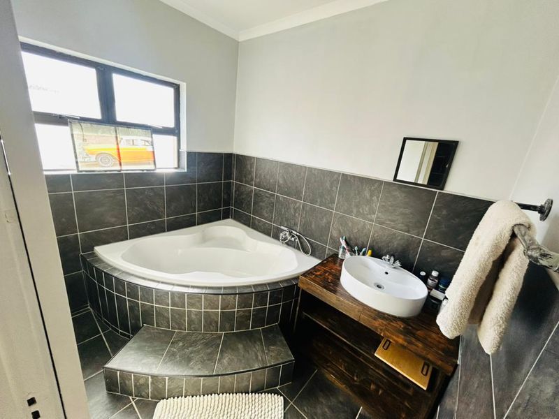 A bathroom featuring a corner bathtub with tiled surround, a vessel sink on a wooden vanity, and dark floor tiles.