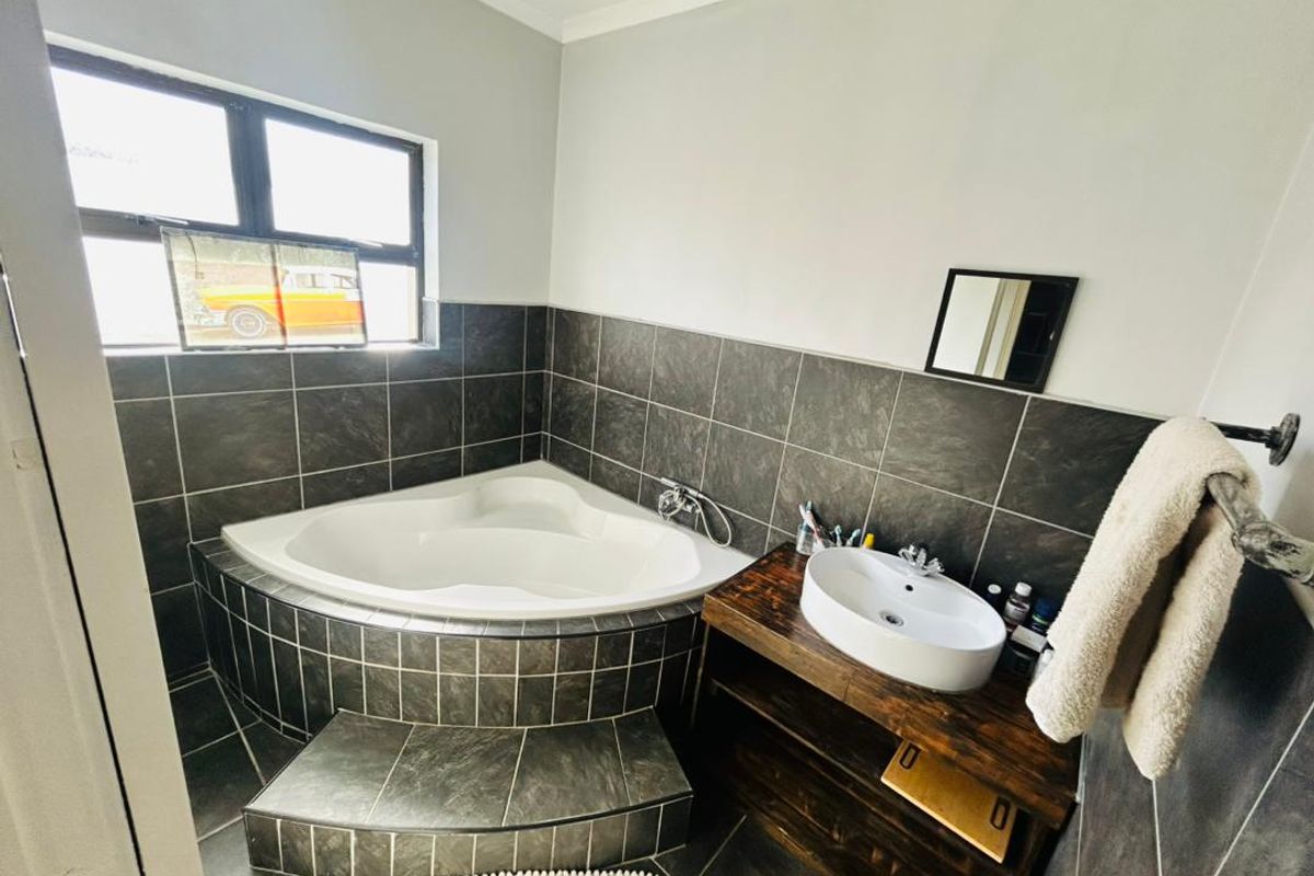 A bathroom featuring a corner bathtub with tiled surround, a vessel sink on a wooden vanity, and dark floor tiles.