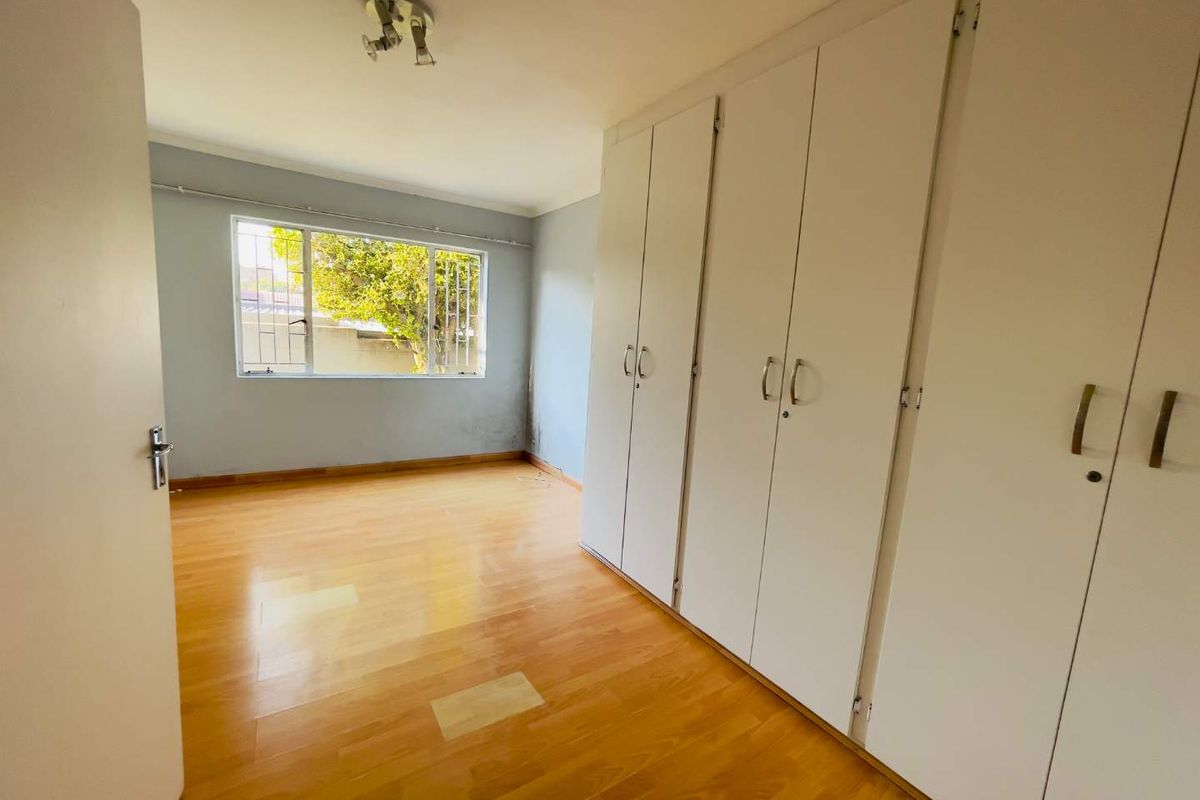 An empty bedroom featuring laminate flooring, built-in cupboards, and a window with security bars.