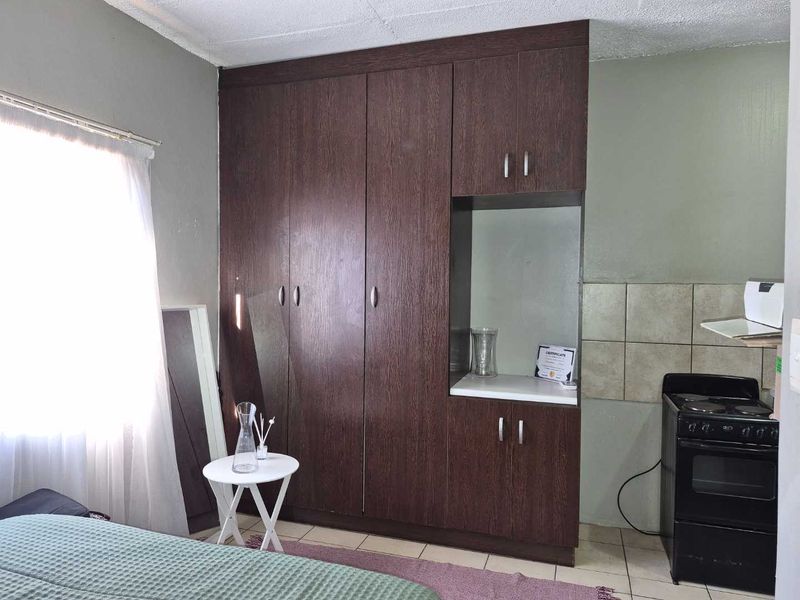 Bedroom featuring dark wood built-in wardrobes, tiled flooring, and a small integrated cooking area with a stove and tiled splashback.