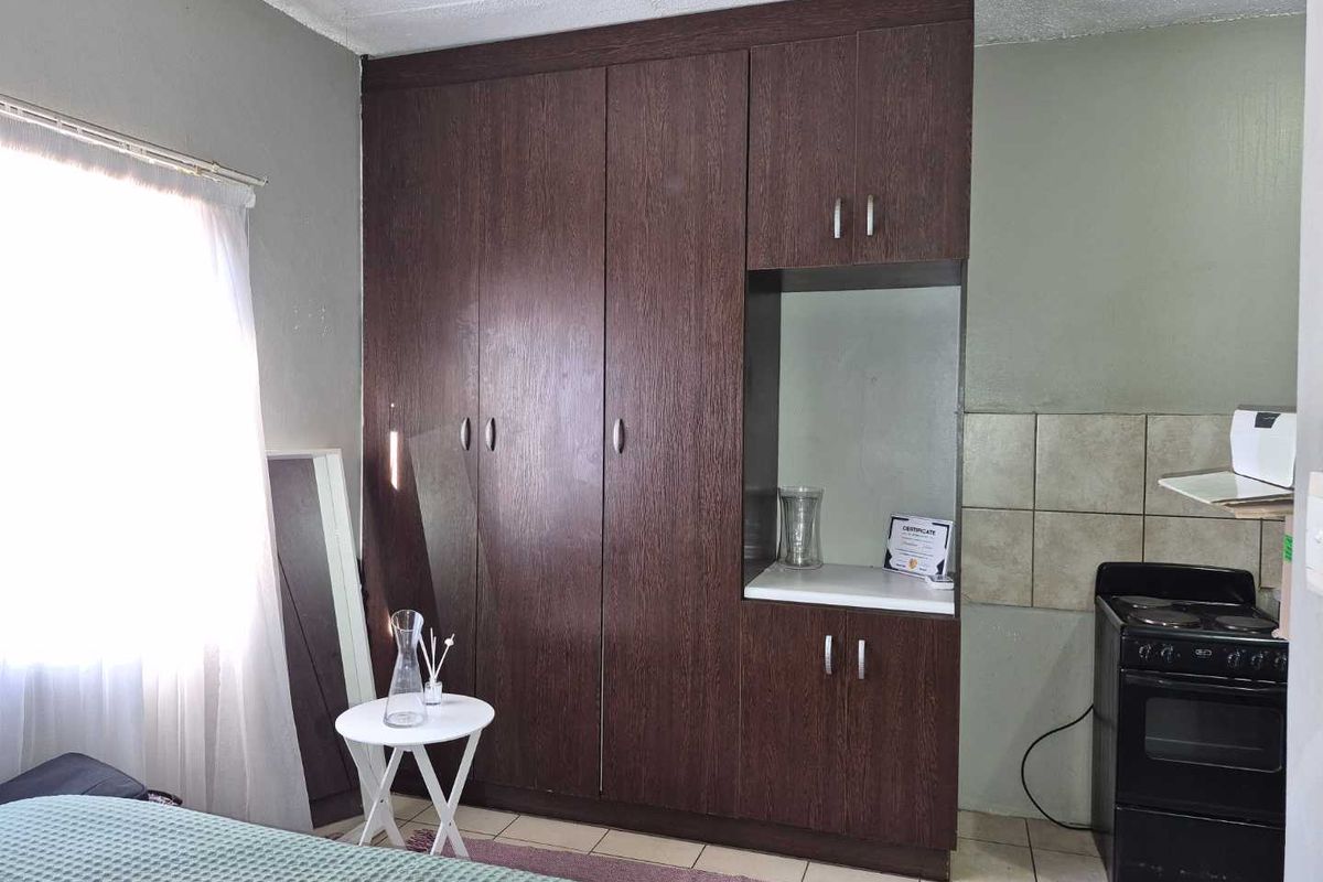 Bedroom featuring dark wood built-in wardrobes, tiled flooring, and a small integrated cooking area with a stove and tiled splashback.