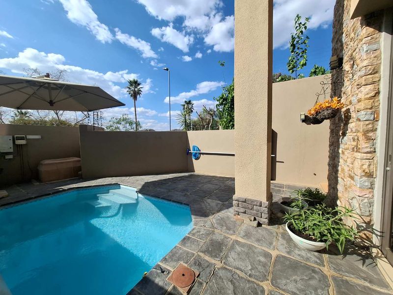A private outdoor pool area featuring stone paving, stone-clad wall accents, and a covered patio section.