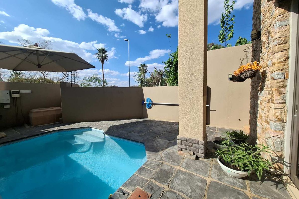 A private outdoor pool area featuring stone paving, stone-clad wall accents, and a covered patio section.