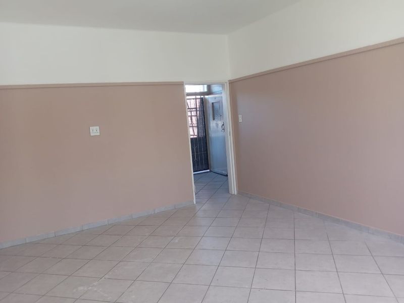An empty living area featuring neutral-toned walls, tiled flooring, and a doorway leading to an exterior security gate.