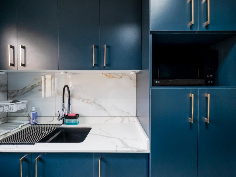 Modern kitchen area featuring dark blue cabinetry, marble-look splashback, stone countertops, and a sleek undermount sink with a gooseneck mixer tap.