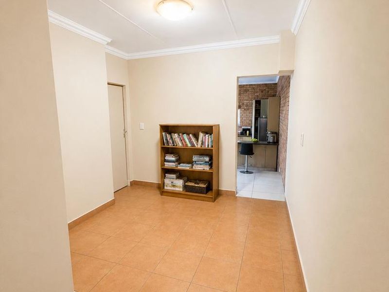 A neutral living area featuring tiled flooring and crown molding, with a clear view through to the adjacent kitchen space.