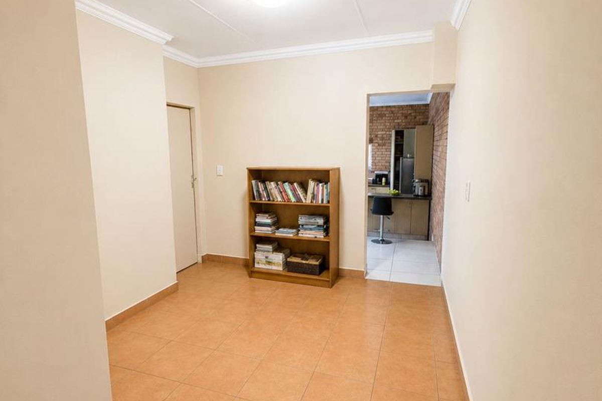 A neutral living area featuring tiled flooring and crown molding, with a clear view through to the adjacent kitchen space.