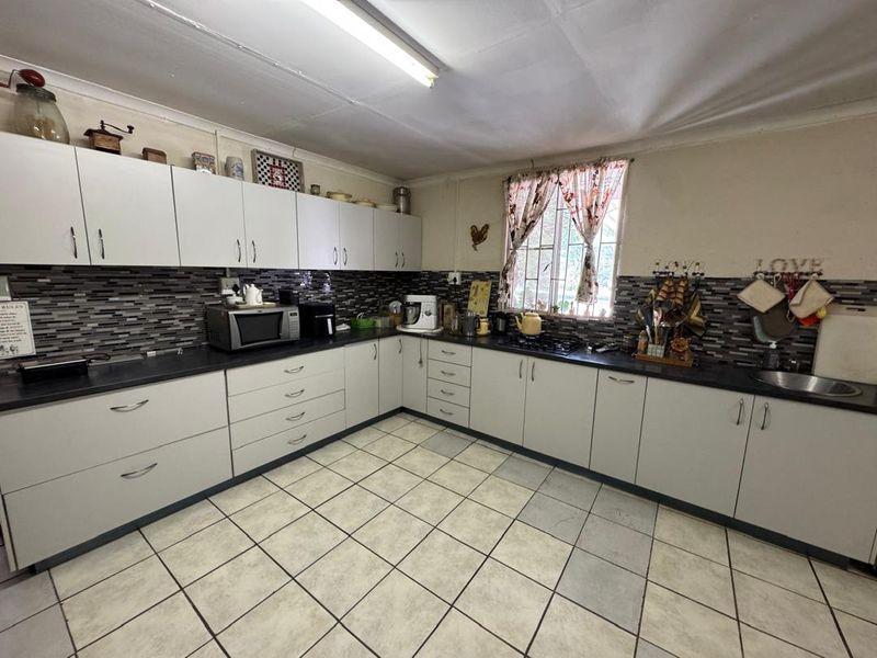 A functional kitchen featuring white cabinetry, mosaic tile backsplash, dark laminate countertops, and ceramic floor tiles, with a window providing natural light.