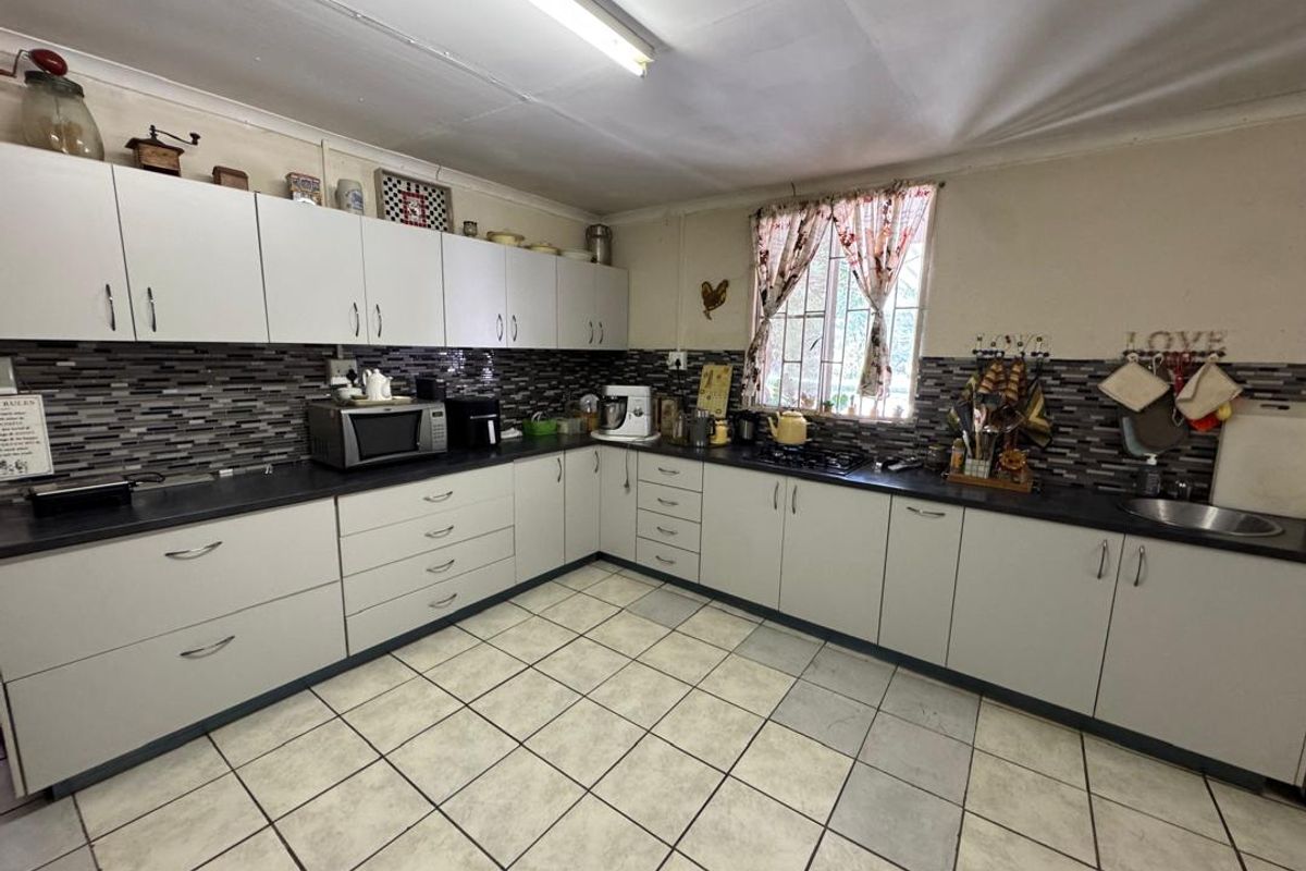 A functional kitchen featuring white cabinetry, mosaic tile backsplash, dark laminate countertops, and ceramic floor tiles, with a window providing natural light.