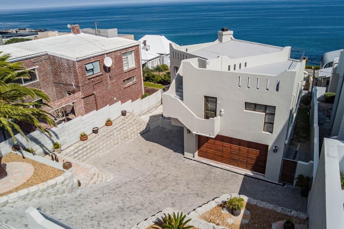 Aerial view of the property featuring a paved driveway, double garage, and exterior staircase, set against a coastal backdrop.